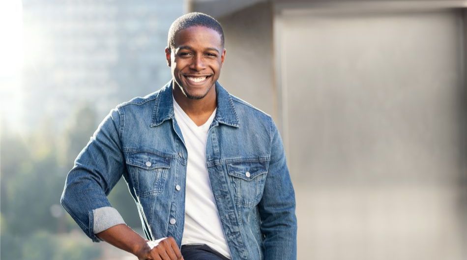 Man in blue denim button up leaning against rail and smiling